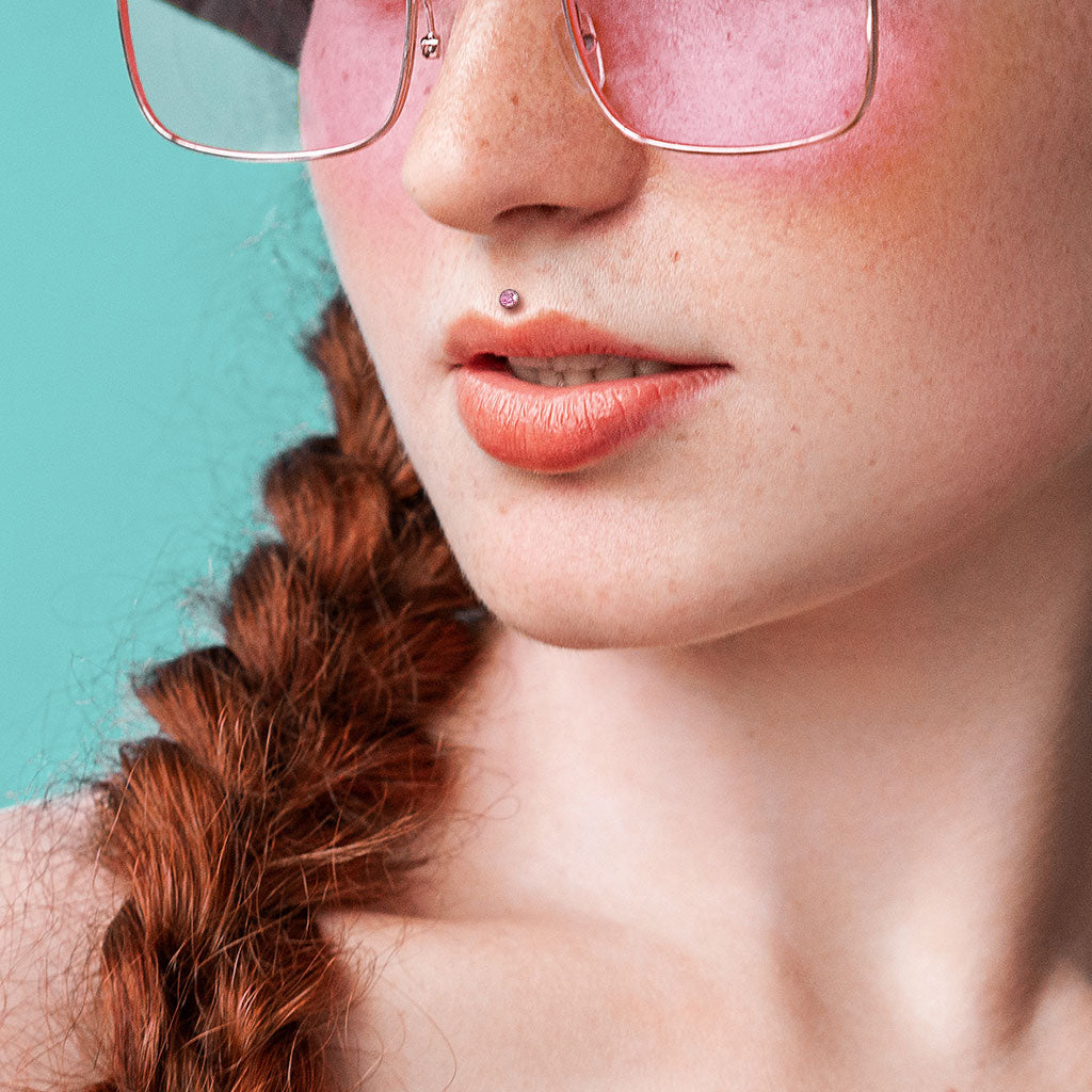 Melchior Jewellery titanium bezel CZ labret on freckled woman with braided red hair and pink glasses