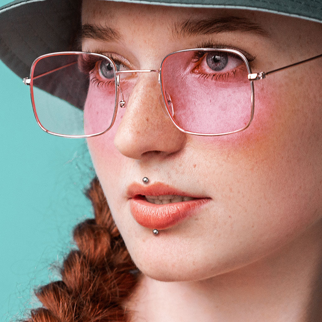 Melchior Jewellery model wearing titanium labret stud push in on upper and lower lip with pink glasses and braided red hair