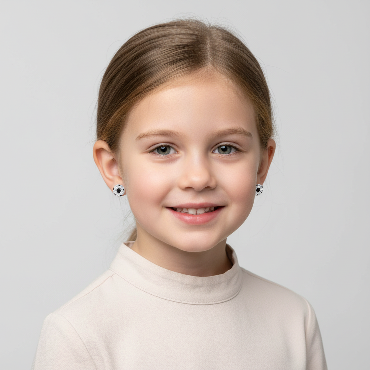 Young girl wearing girls sterling silver football earrings by Melchior Jewellery with a white top