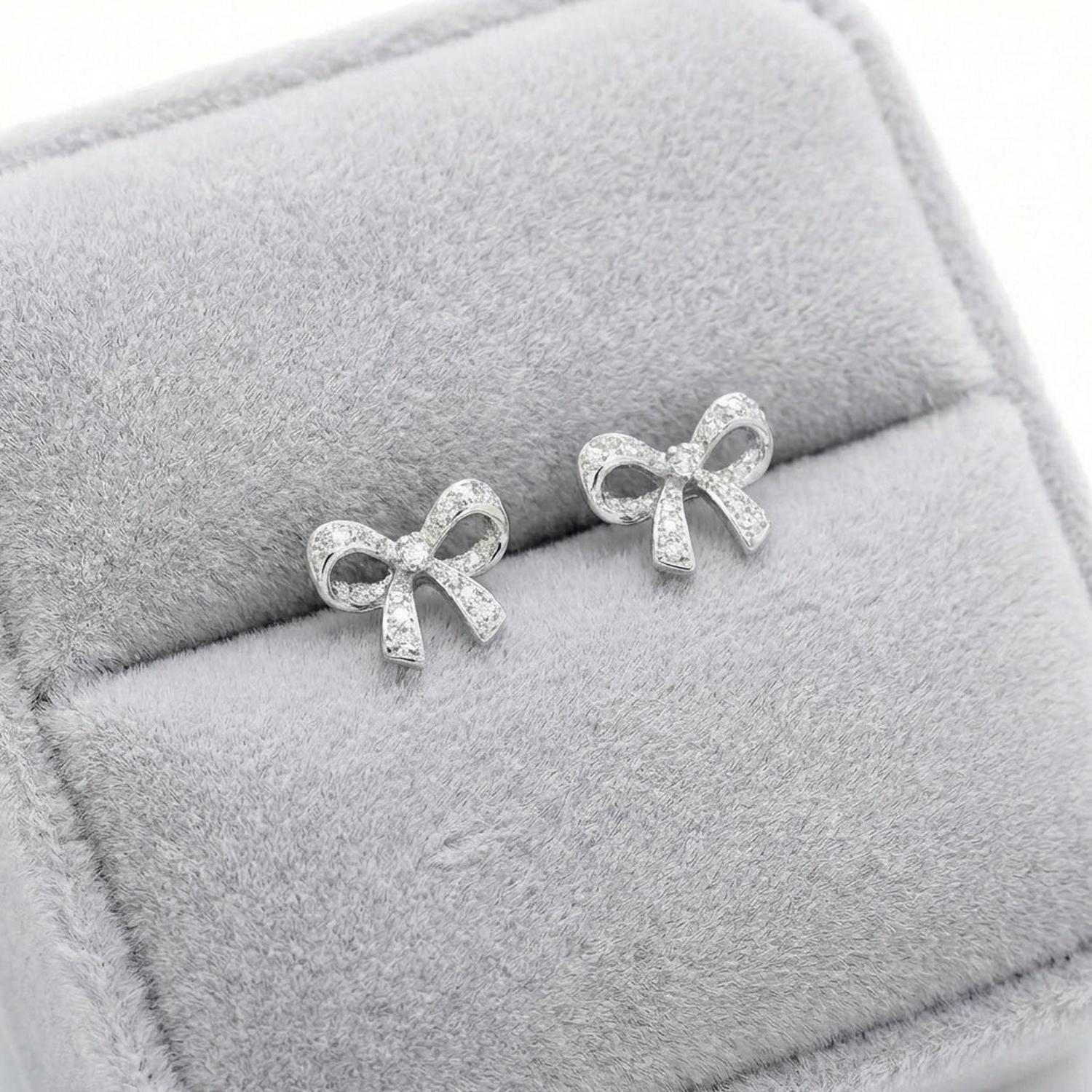 Sentiell sterling silver bow stud earrings with delicate design displayed on grey velvet cushion