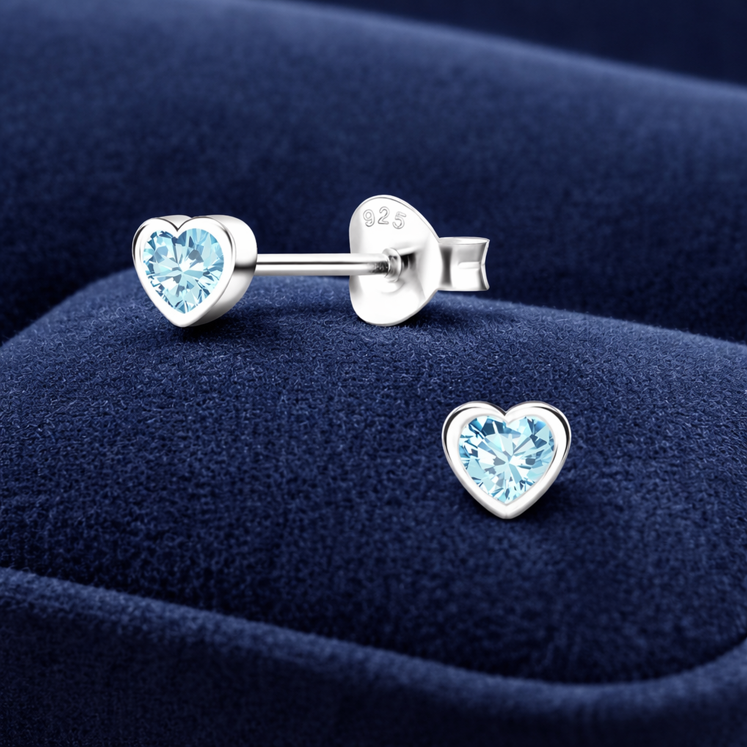 Sterling silver childrens aquamarine heart earrings with blue gemstones on navy velvet background