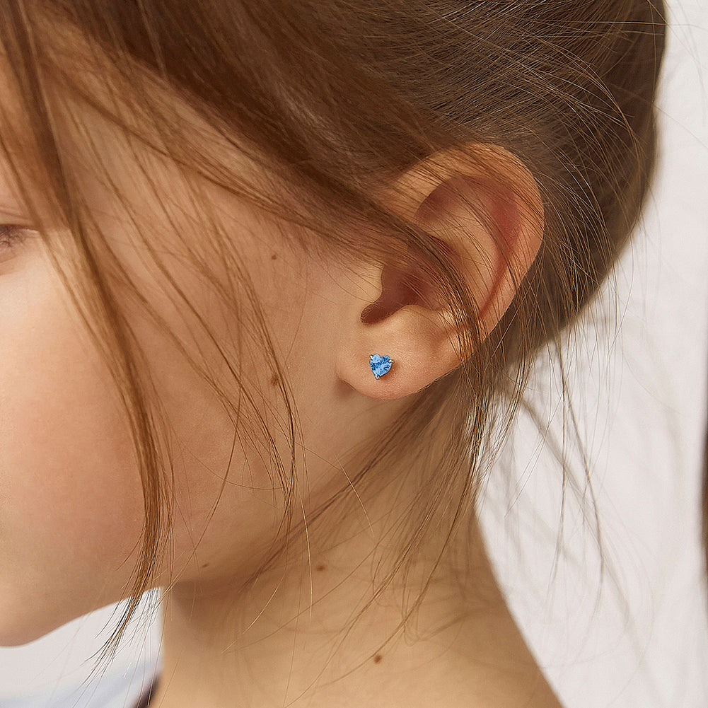 Child wearing blue heart-shaped sterling silver screw back earrings for girls from In Season Jewellery