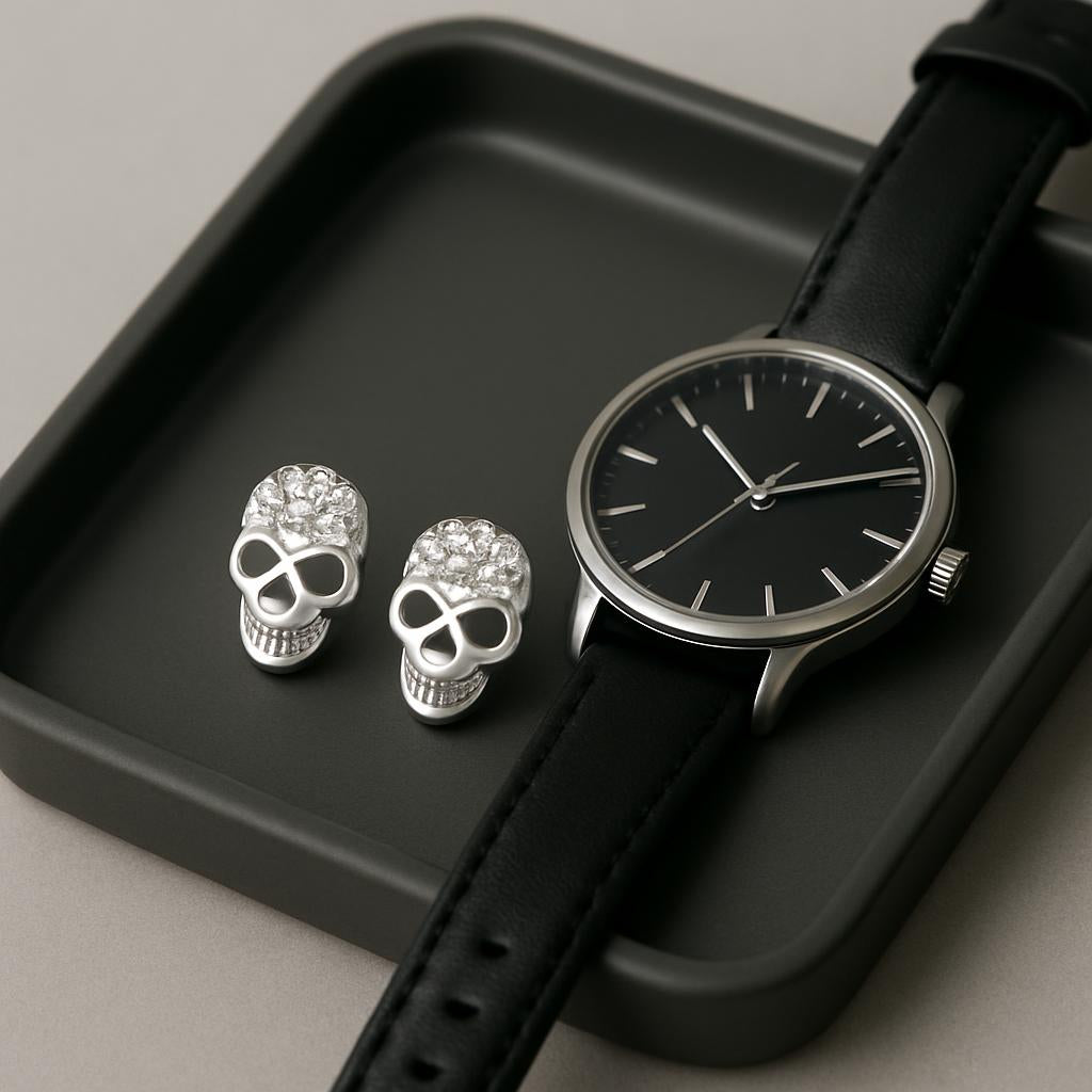Sterling silver skull stud earrings by Melchior Jewellery displayed next to black leather strap watch