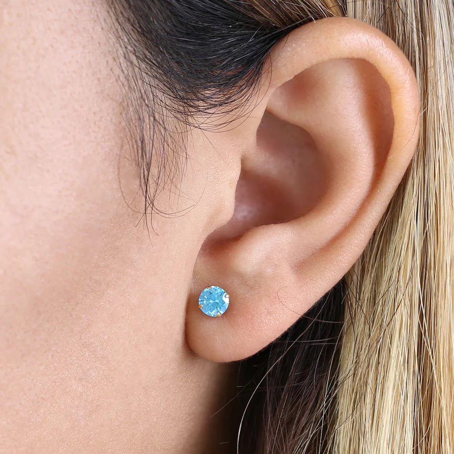 14k yellow gold blue topaz earrings worn on ear showcasing bright blue gemstone studs by Melchior Jewellery