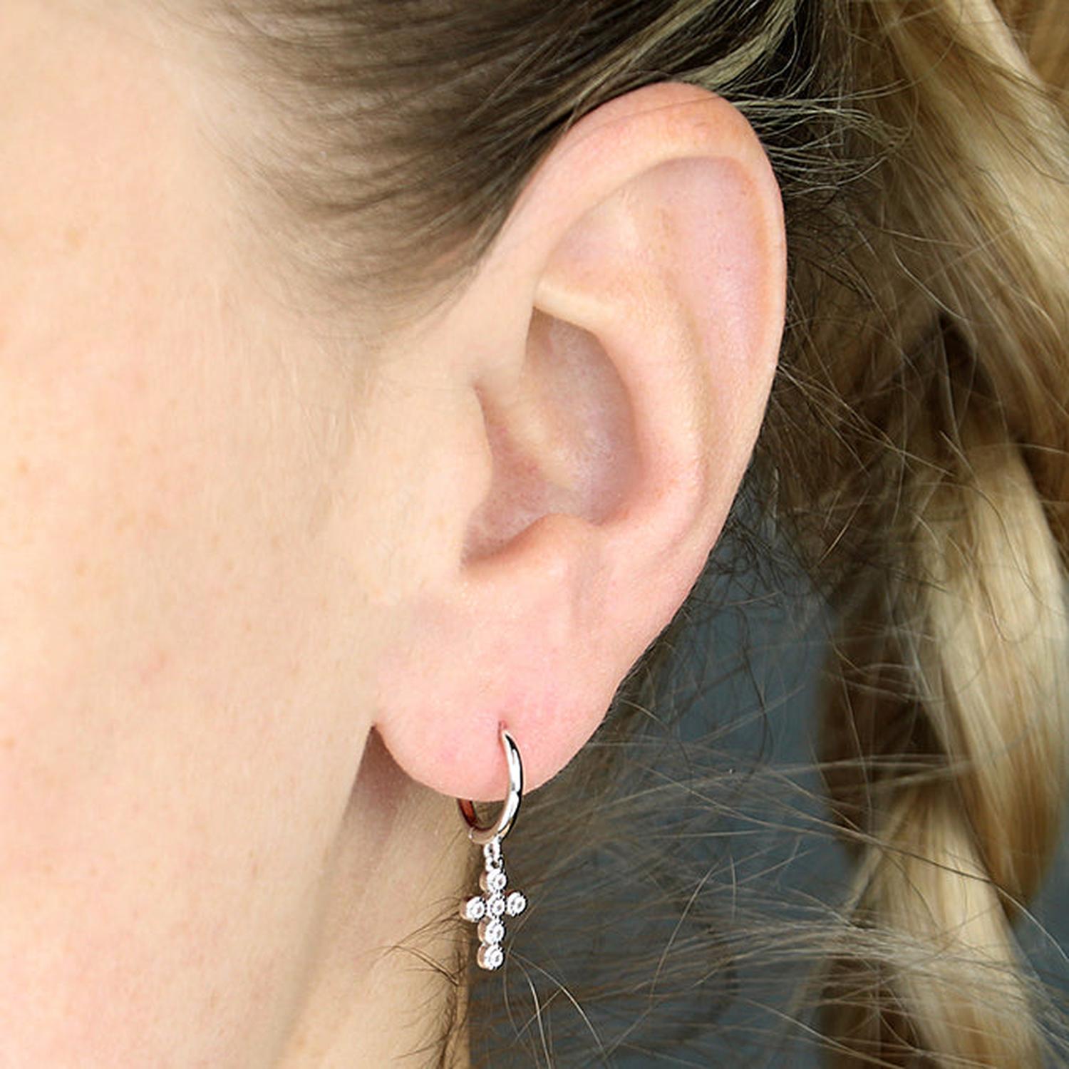 Melchior Jewellery silver huggie hoop earrings with small dangling crystal cross charm on ear