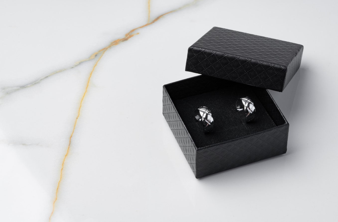 Shiny silver cufflink style earrings for men displayed in a black textured gift box, best silver earrings for men 2024