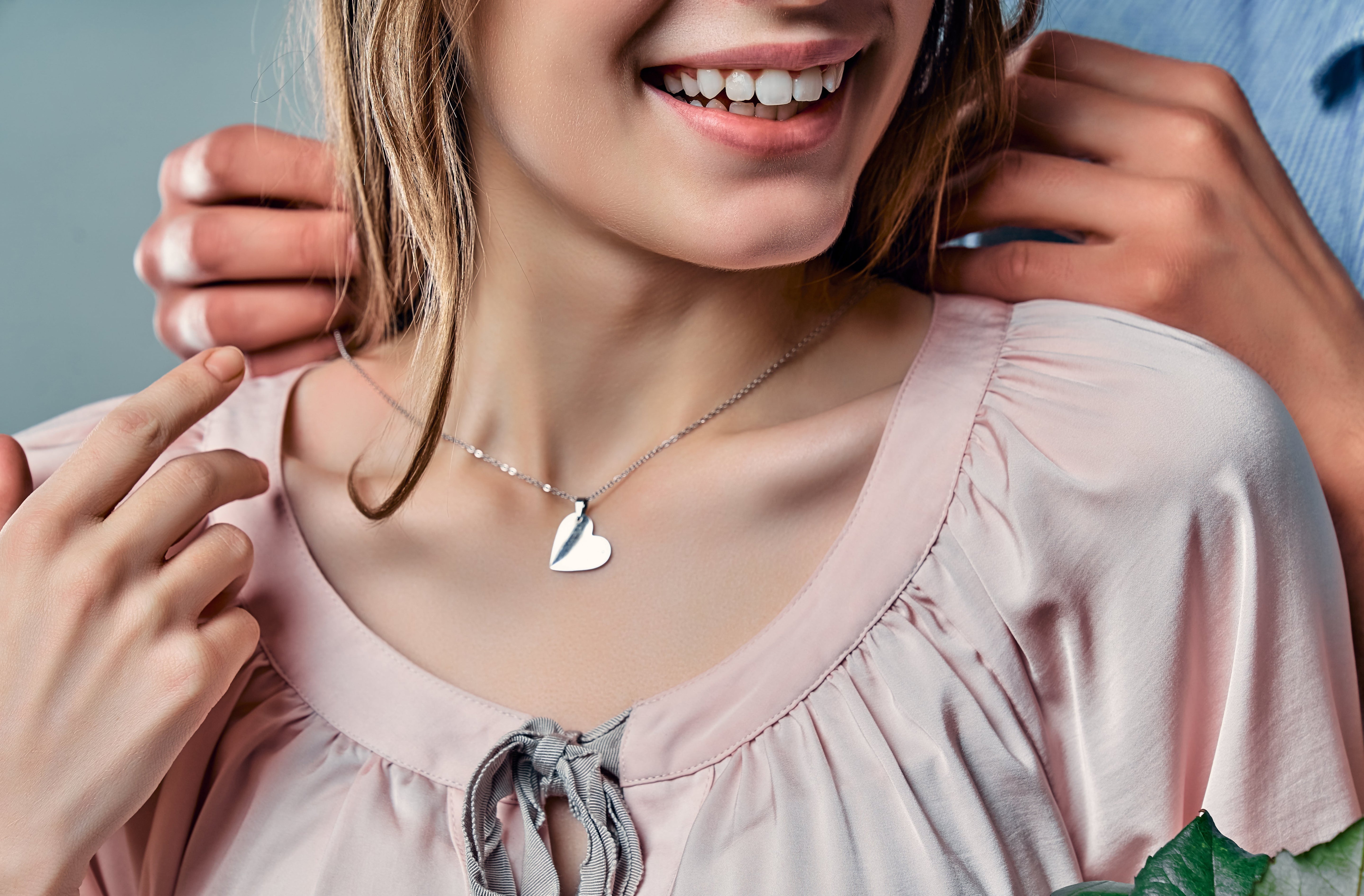 Smiling girl wearing an elegant sterling silver necklaces for kids with a shiny heart pendant and soft pink blouse