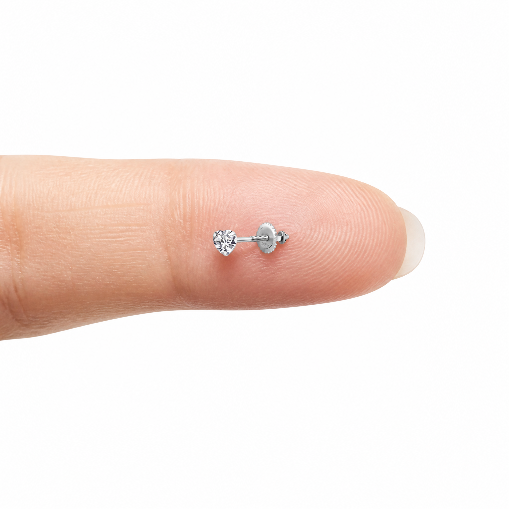 A tiny silver-toned labret stud earring with a clear heart-shaped gemstone, shown resting on the tip of a human finger for scale against a plain white background.
