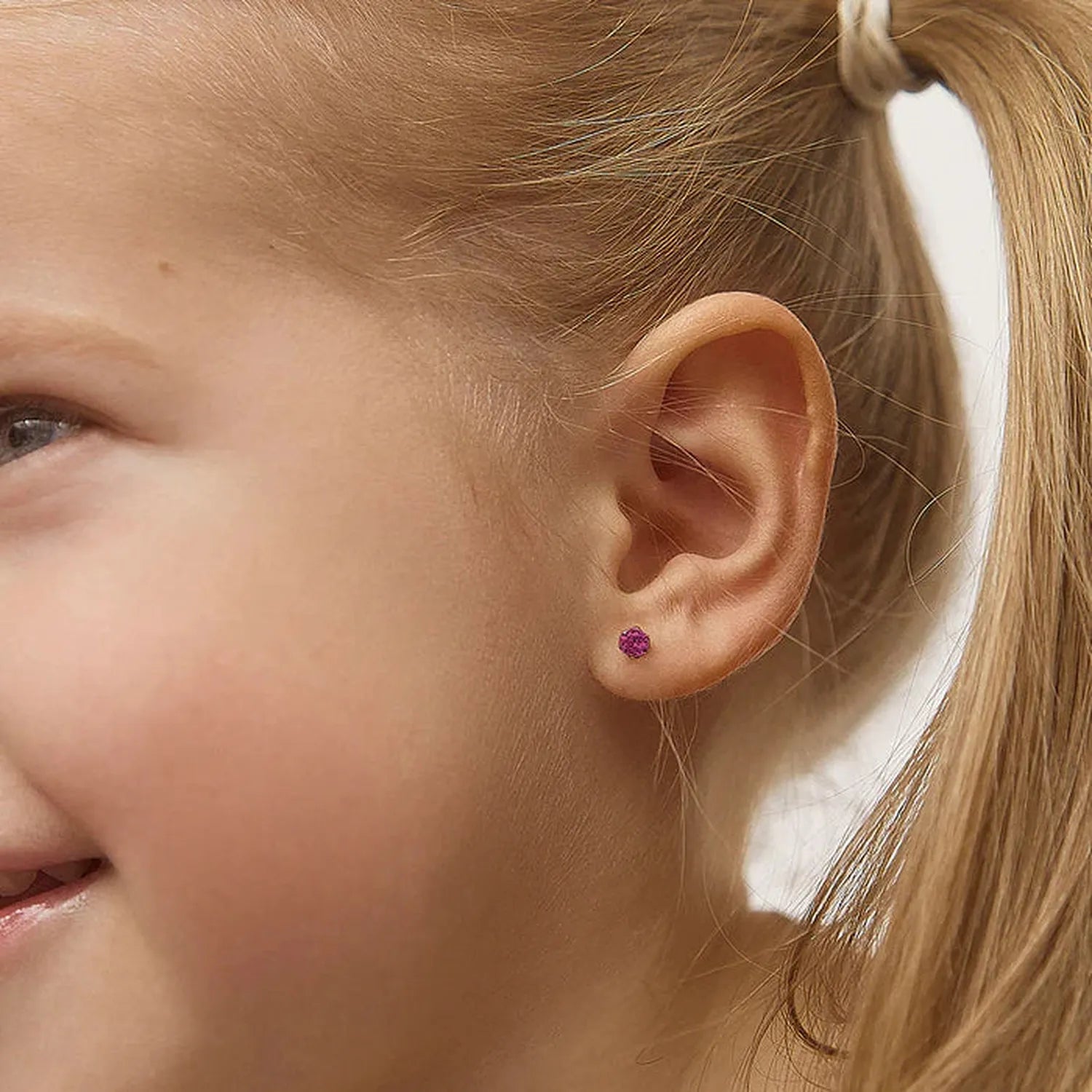 Child wearing 14k gold July birthstone earrings by In Season Jewellery showing small purple gemstone studs