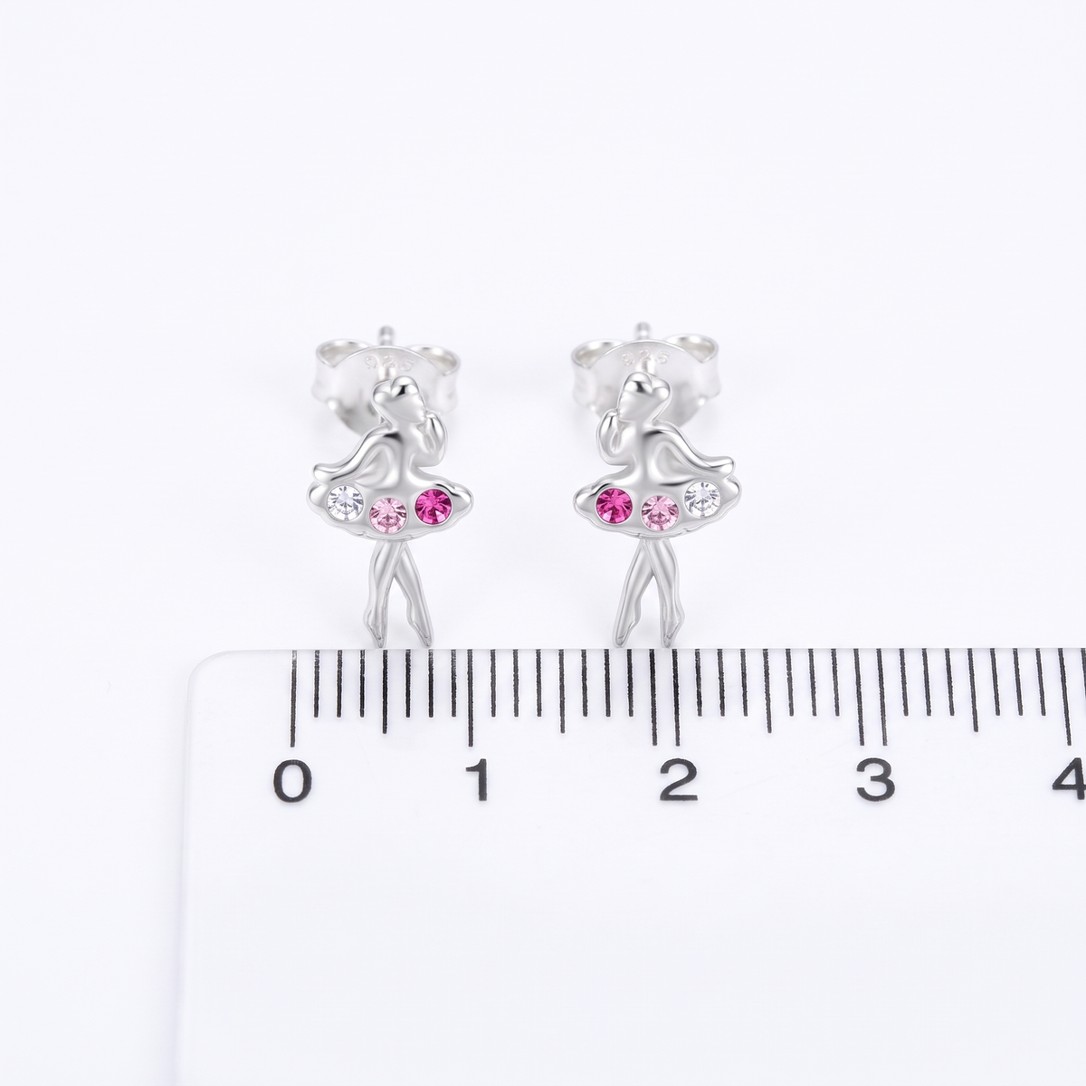A pair of silver ballerina stud earrings with pink gemstone accents, shown above a white ruler for scale