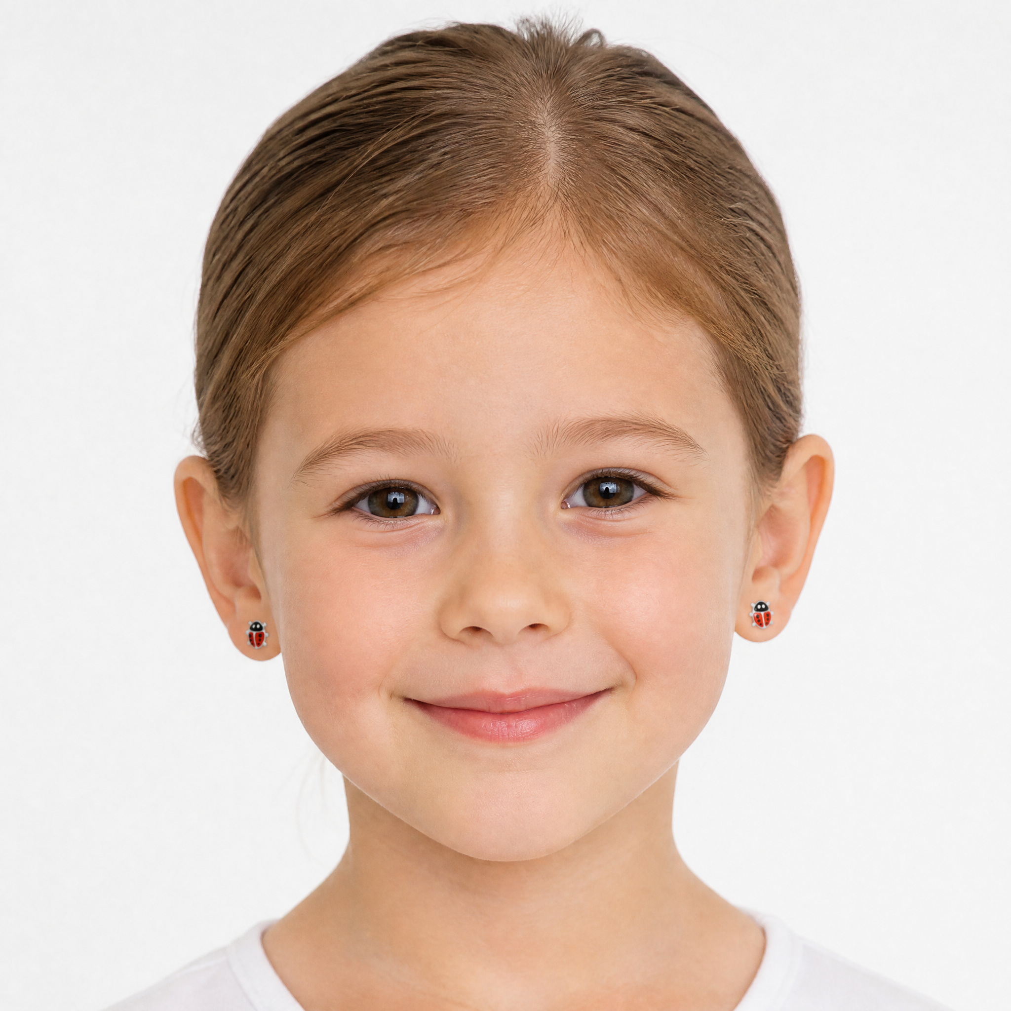 A young girl with light brown hair wearing small red and black ladybug stud earrings, shown in a clean studio portrait against a white background.