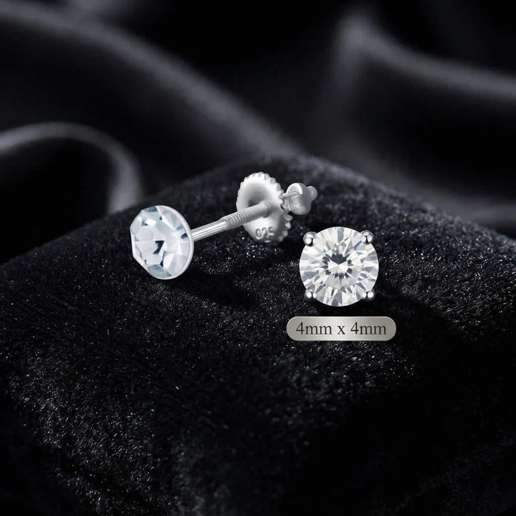 A pair of silver stud earrings with round clear gemstones, displayed on a black velvet surface. One earring is shown from the side, revealing the post and butterfly back, while the other is shown from the front.