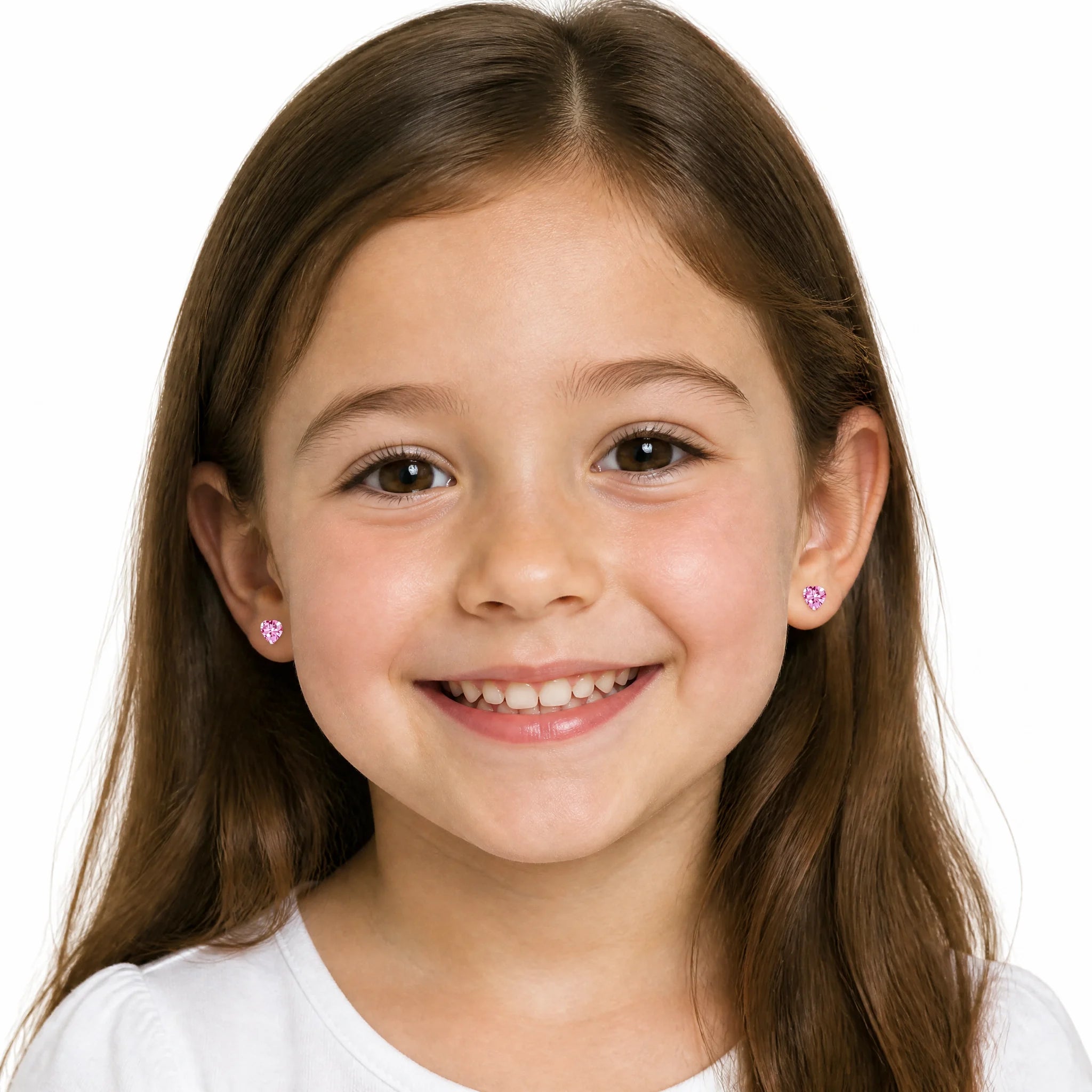 A young girl with long brown hair smiling at the camera, wearing small pink heart-shaped stud earrings against a plain white background.