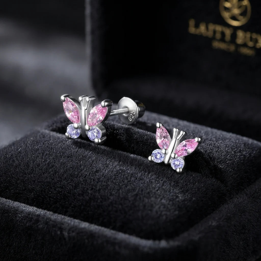 A pair of silver butterfly stud earrings with pink marquise-cut stones and small round purple stones, displayed in a black velvet jewelry box. The brand name 'LATTY BUN' is visible on the inner lid.