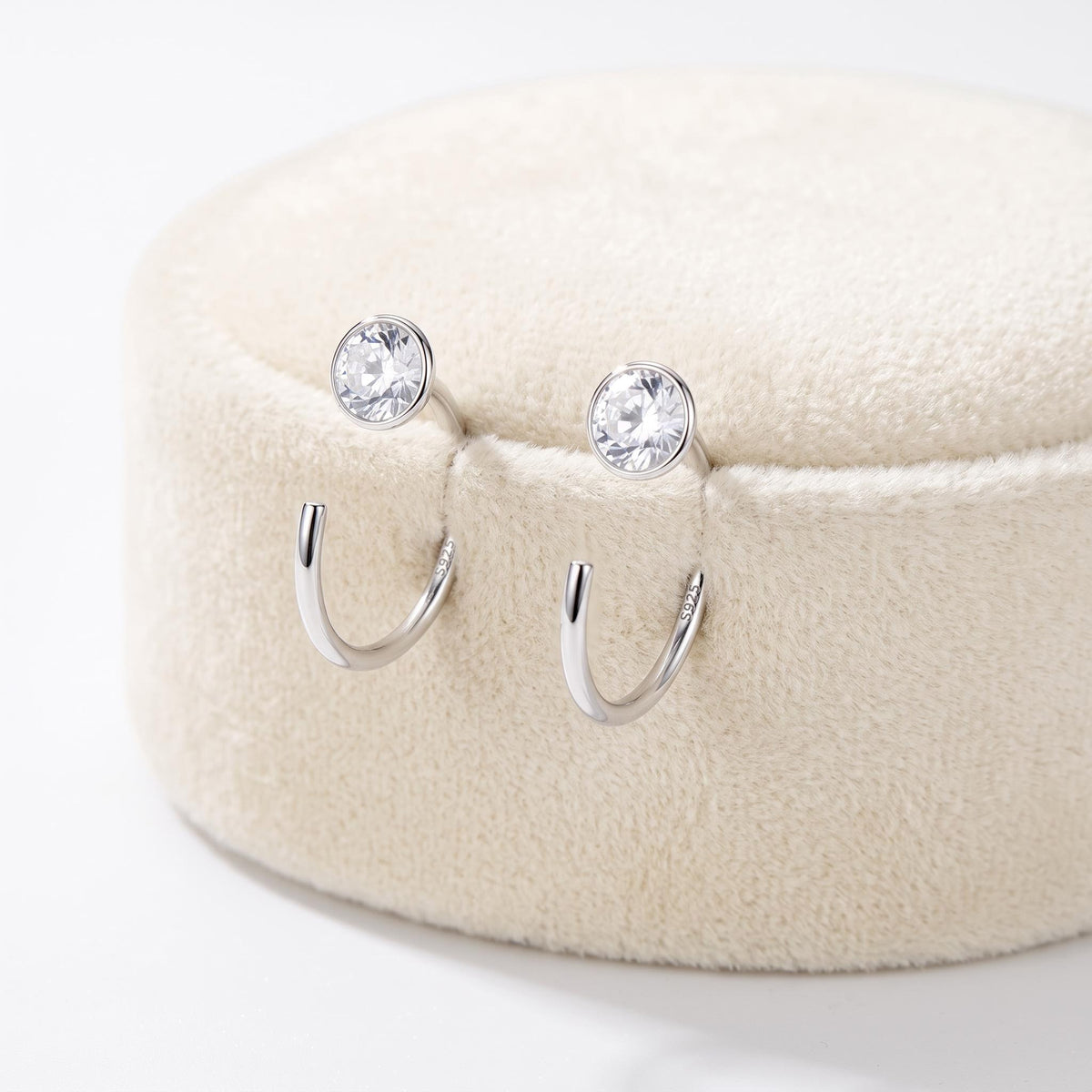 A pair of silver pull through hoop earrings with round clear gemstones