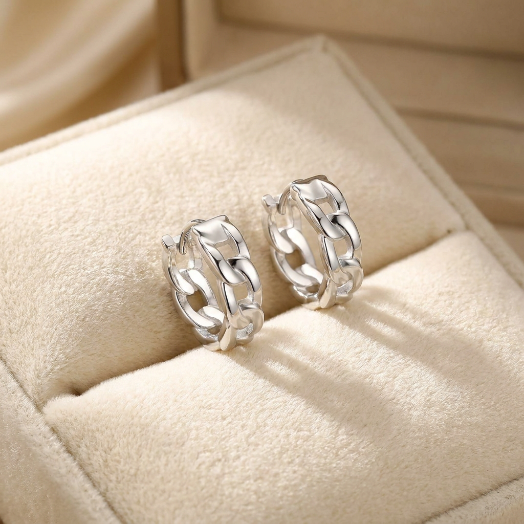 A pair of polished silver huggie hoop earrings with a textured, wavy interlocking design, displayed on a beige velvet jewelry box.