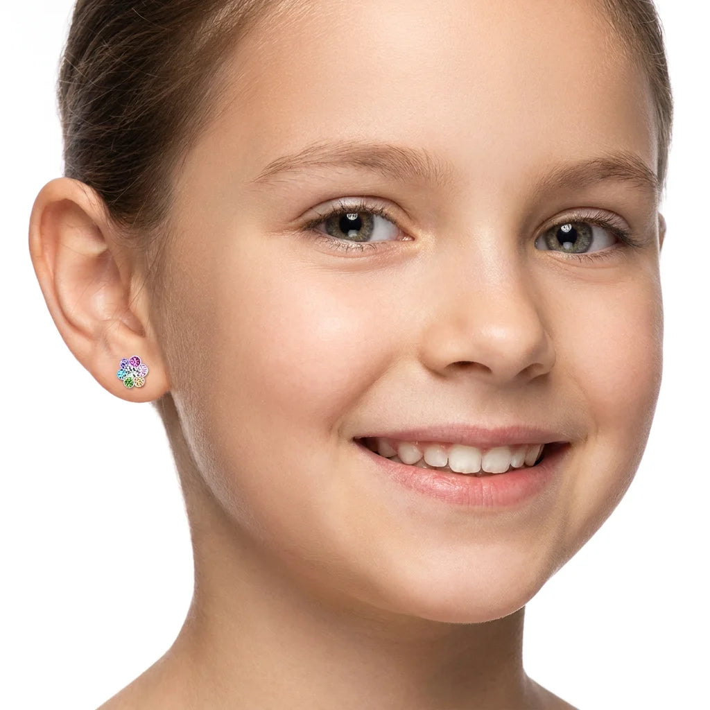 A close-up of a smiling young girl wearing a small colorful flower-shaped stud earring on her ear, against a clean white background.
