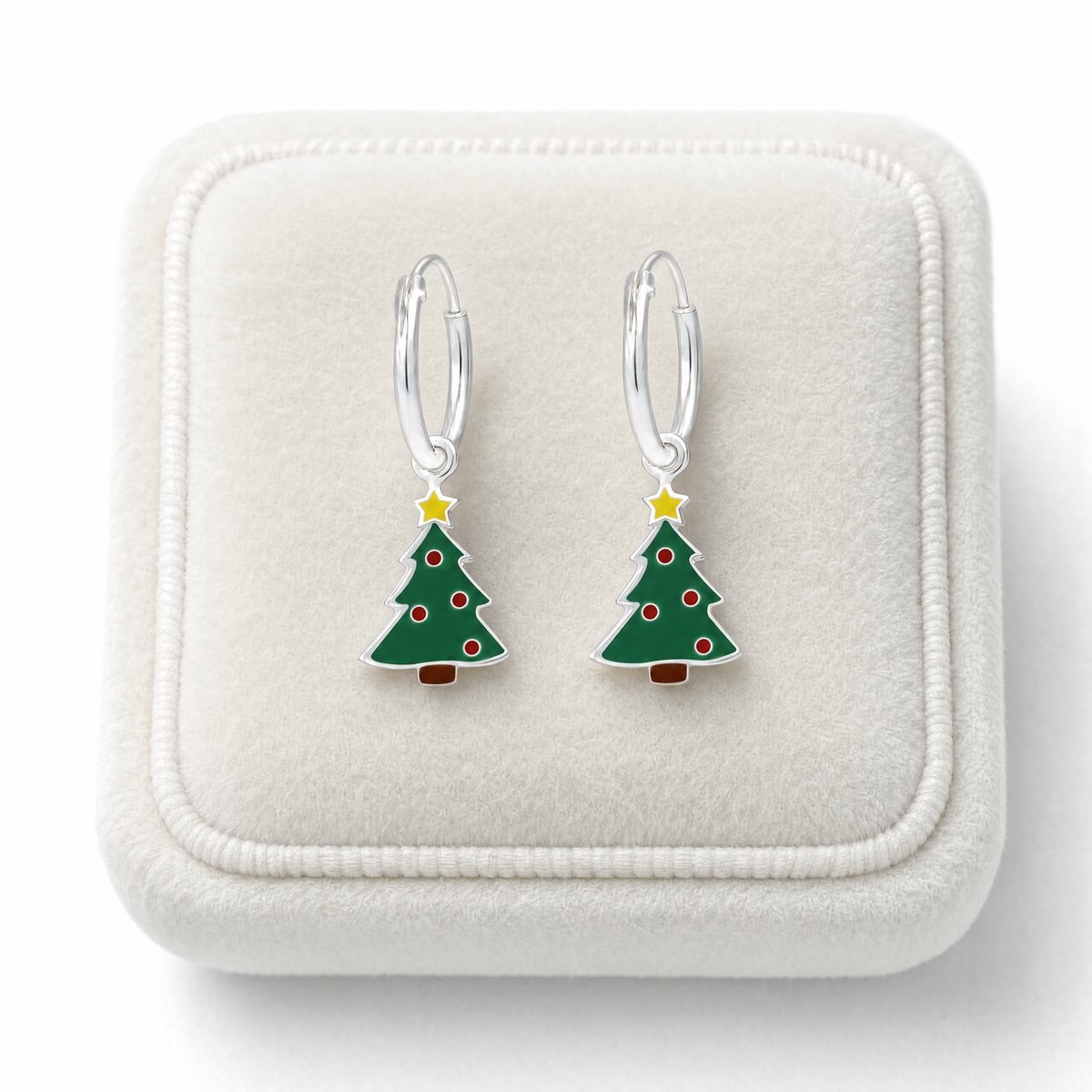 A pair of silver hoop earrings with dangling Christmas tree hoop earrings, displayed on a cream jewellery cushion