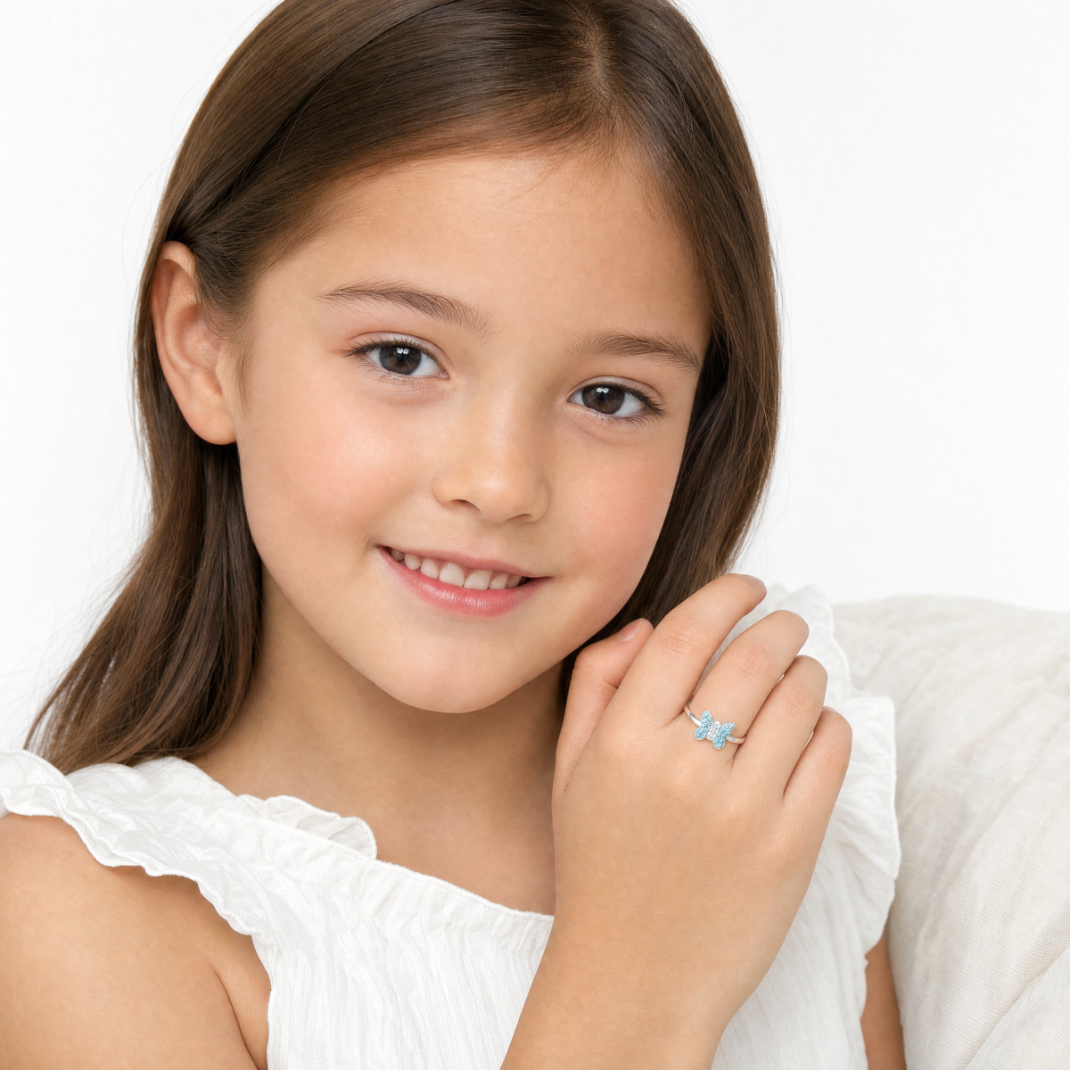 A young girl with long brown hair smiles while wearing a silver ring with a light blue butterfly design on her finger.