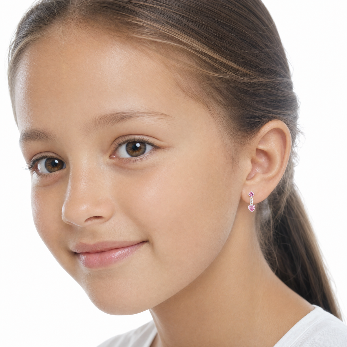 A close-up portrait of a young girl with brown hair in a ponytail, wearing a small pink and silver dangle heart earring 