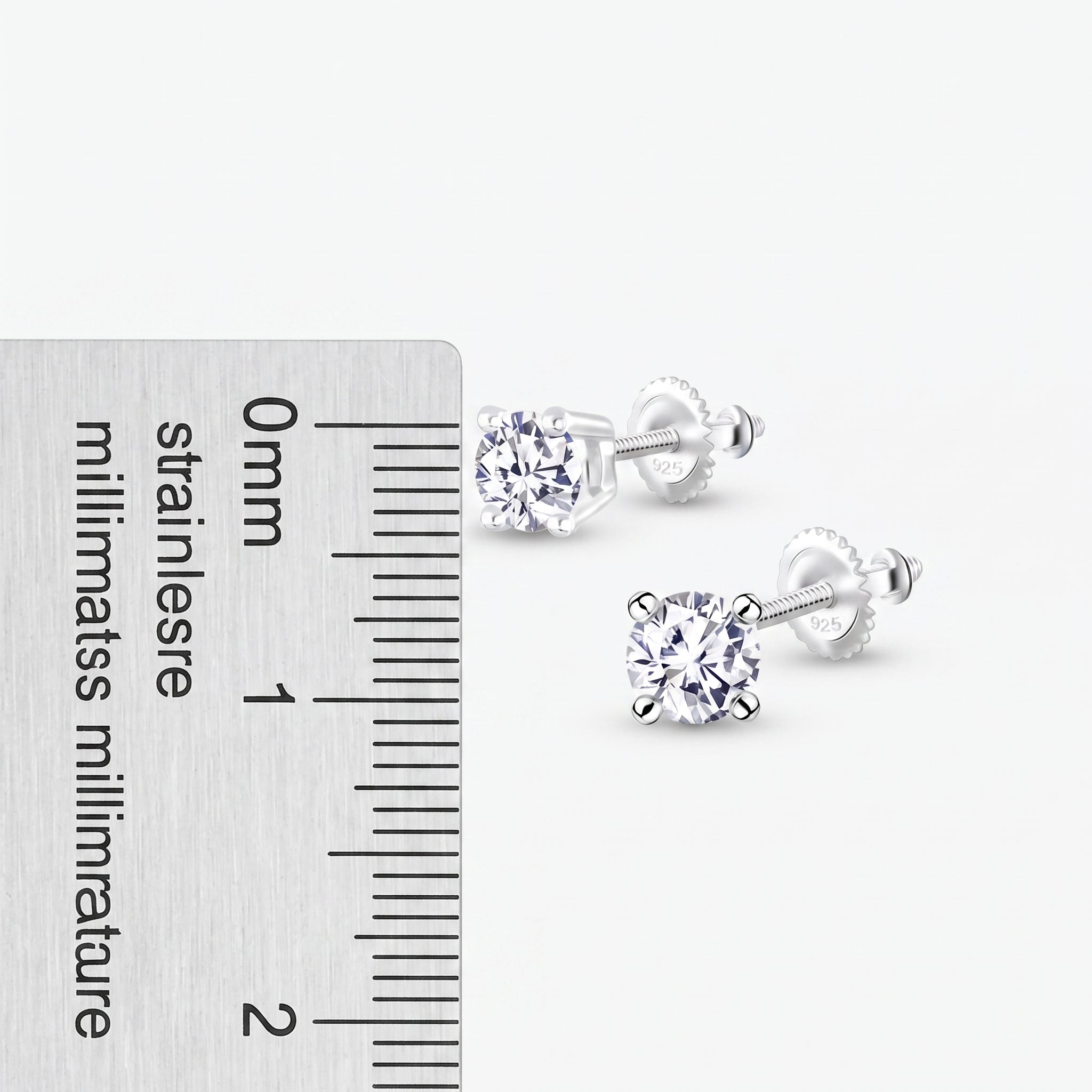 A pair of silver stud earrings with round clear gemstones, shown next to a stainless steel millimeter ruler for scale on a light gray background.