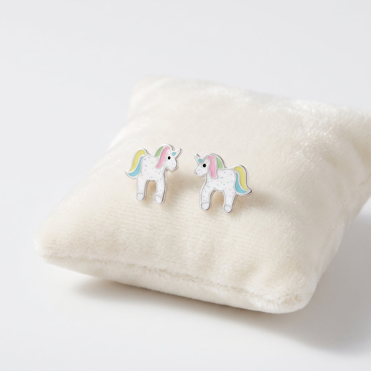 A pair of small unicorn stud earrings with white bodies, pastel rainbow manes and tails