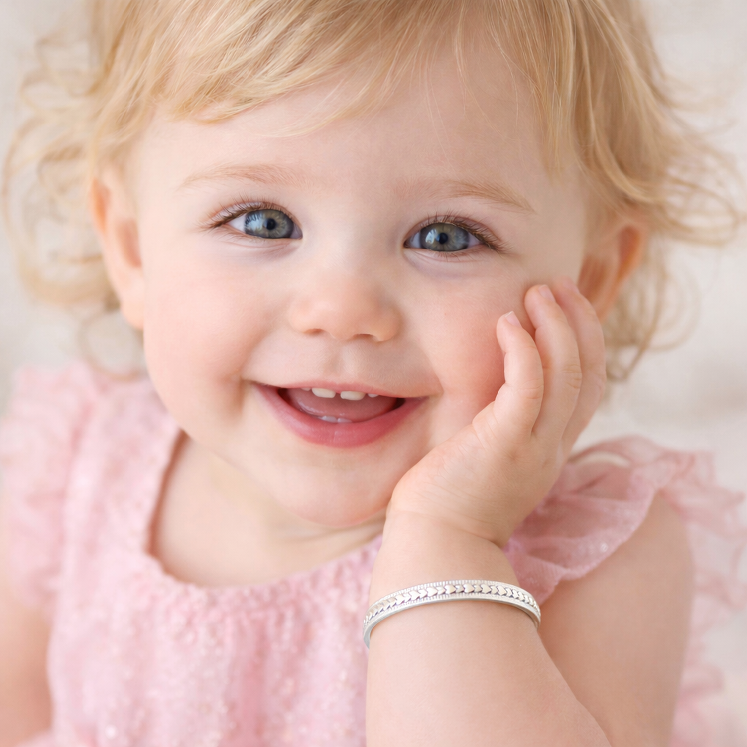 Smiling baby girl wearing Melchior Jewellery's expandable heart baby bracelet in silver on her wrist