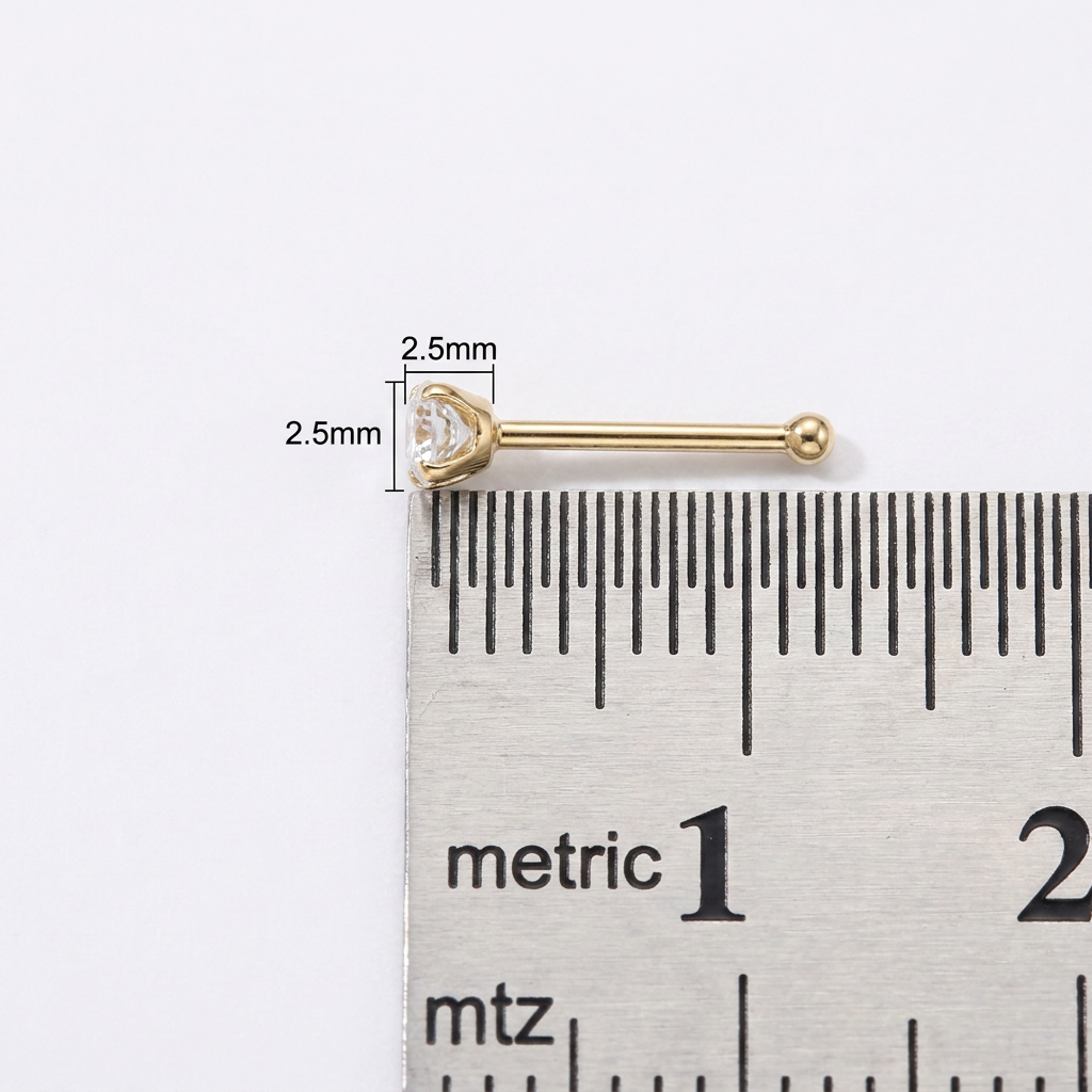 A gold barbell stud earring with a clear heart-shaped gemstone, shown next to a metal ruler with 2.5mm dimension markings on a white background.
