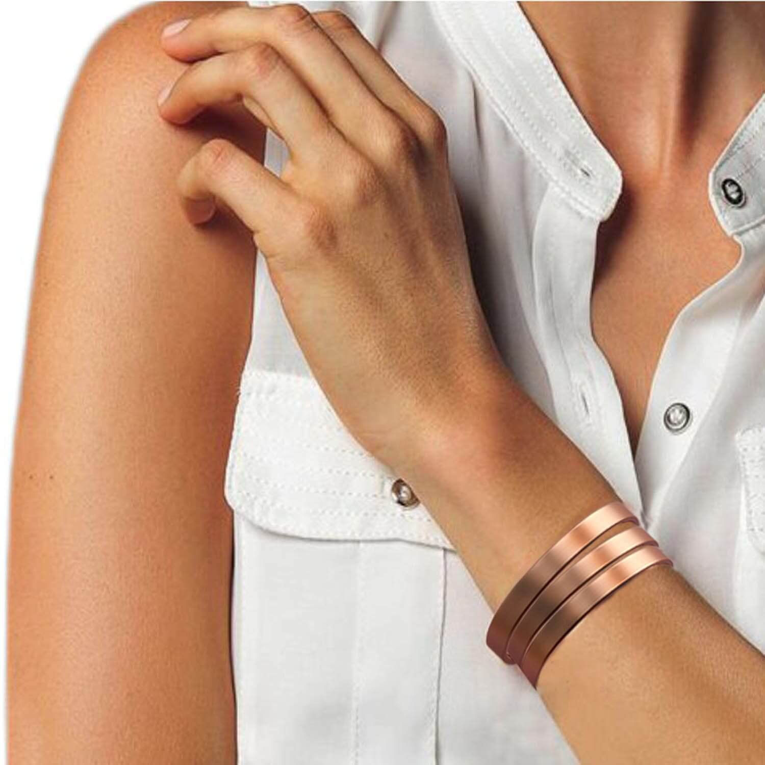 Woman wearing three slim copper bracelets on wrist with white blouse showcasing magnetic copper therapy bangle for joint relief