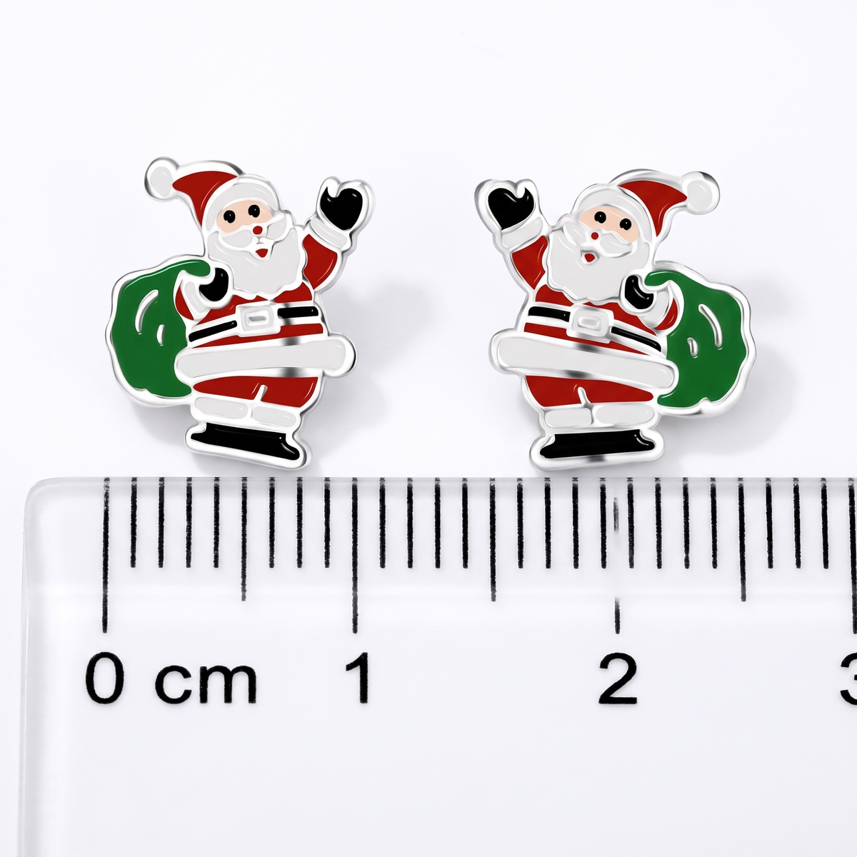 A pair of small Santa Claus stud earrings with a sterling silver and colorful enamel details, shown above a clear ruler for scale 