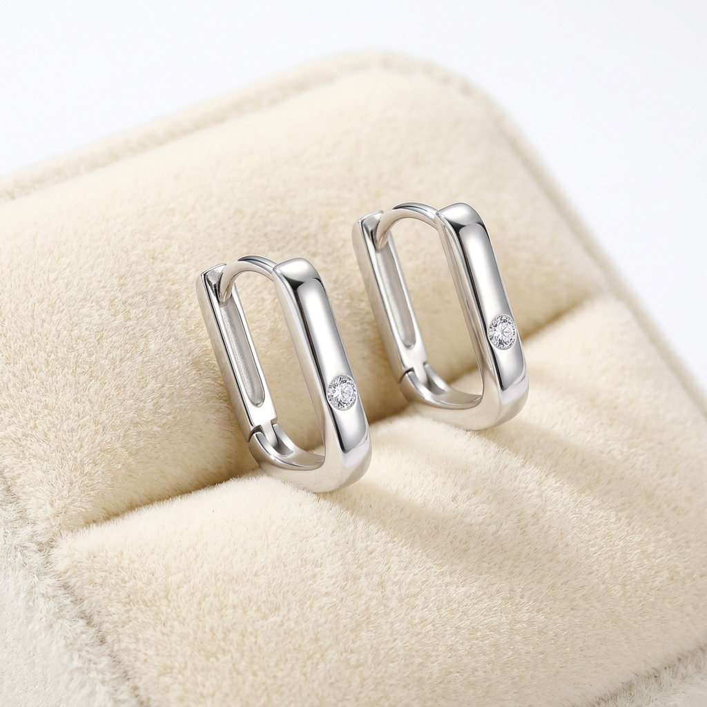 Silver hoop earrings with a sparkling diamond accent, elegantly displayed on a soft cushion.
