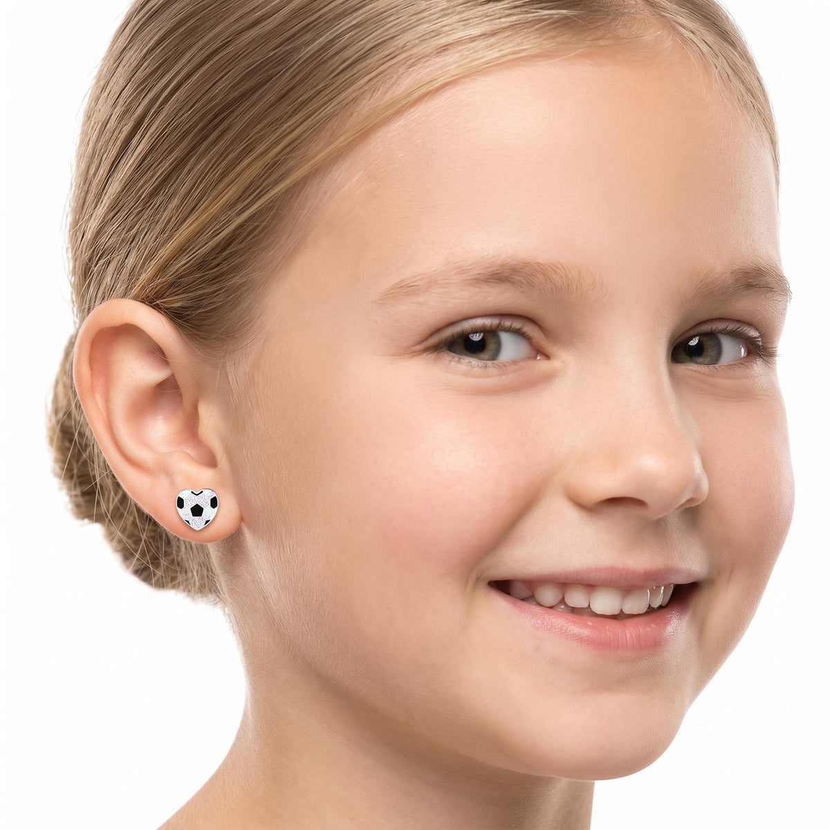 A close-up of a young girl with blonde hair pulled back, wearing a small black and white soccer ball stud earrings
