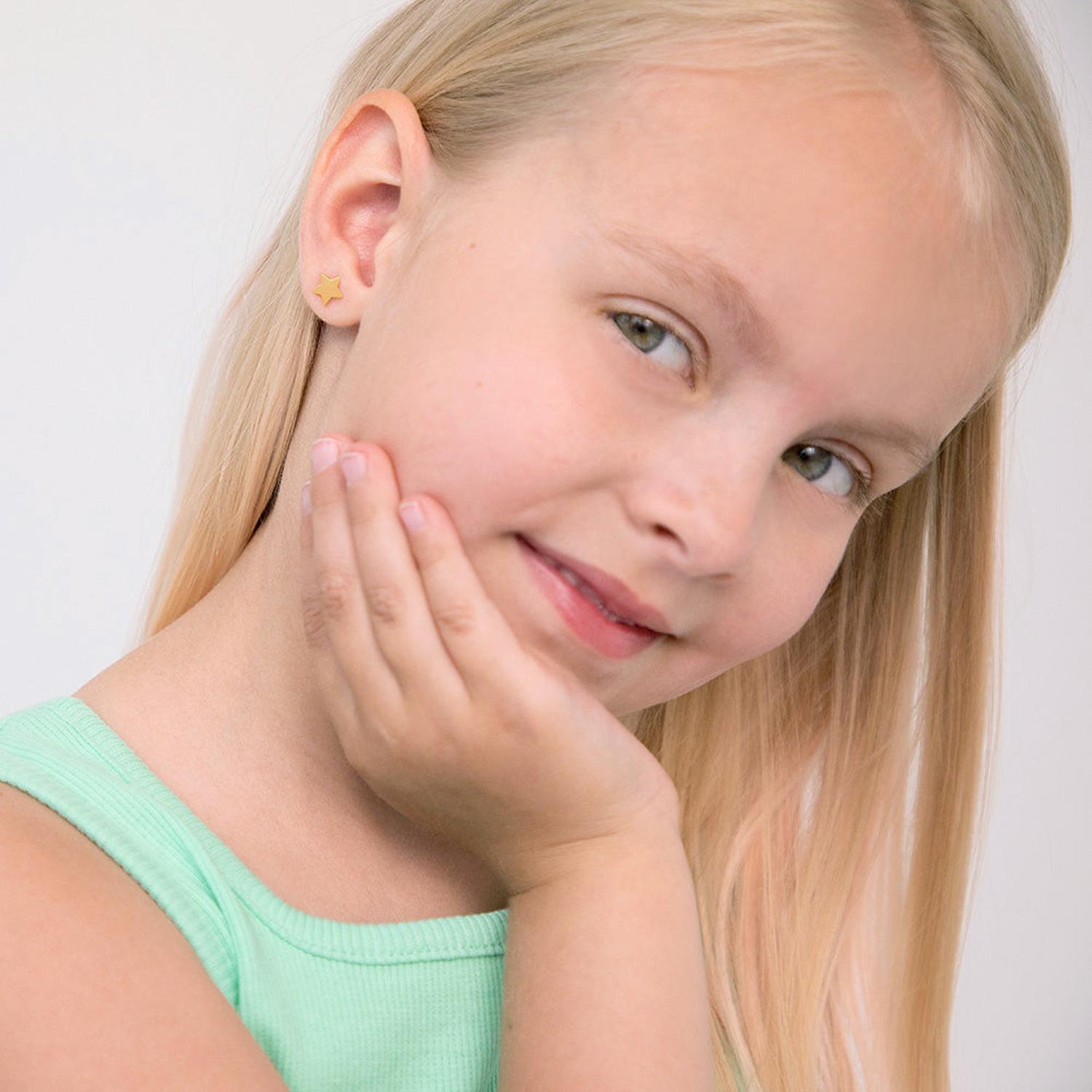 Young girl wearing 14k gold star stud earrings for girls with smooth shiny finish, smiling and wearing a light green top
