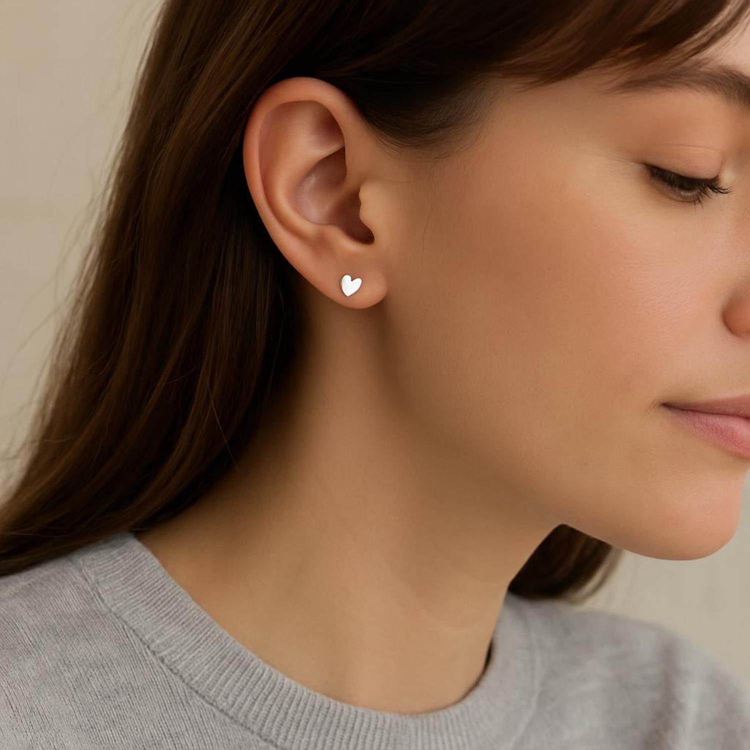 Melchior Jewellery titanium heart stud earrings worn by woman with brown hair and grey top
