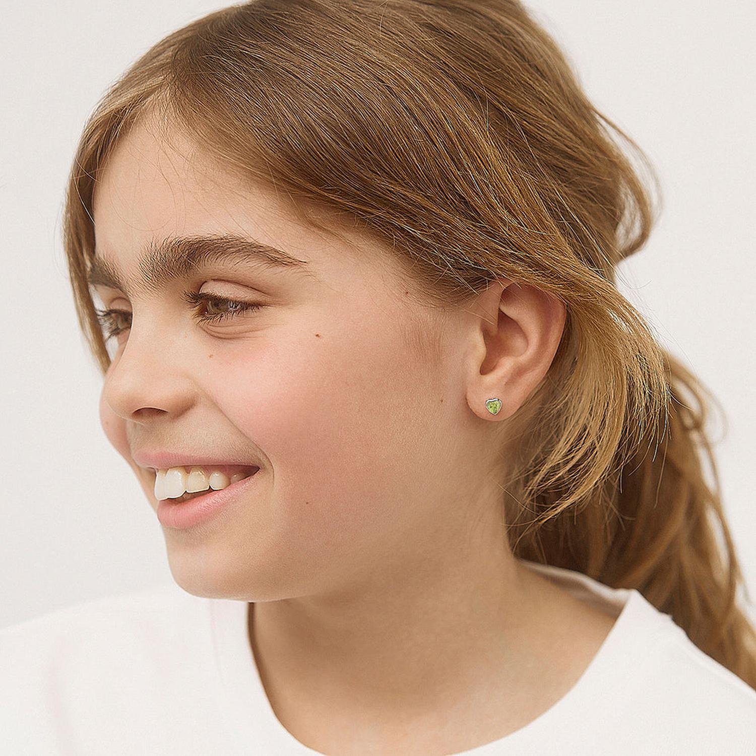 Young girl wearing delicate green heart-shaped Girls August Birthstone Earrings from In Season Jewellery