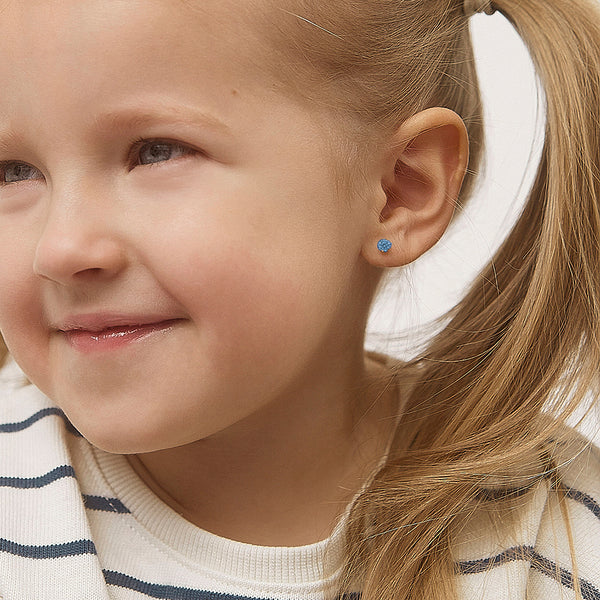 Child wearing 14k gold December birthstone earrings with blue gemstone studs by In Season Jewellery