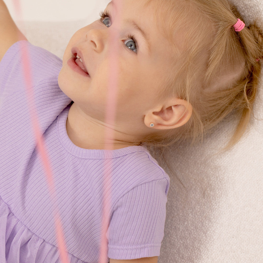 Young girl wearing 14k gold girls screw back earrings from In Season Jewellery lying down in a purple dress