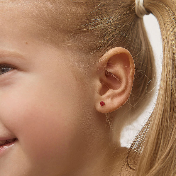 Close-up of child wearing 14k gold January birthstone earrings with red gemstone studs from In Season Jewellery