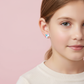 Young girl wearing kids winged unicorn screw back earrings from Melchior Jewellery with pastel pink background