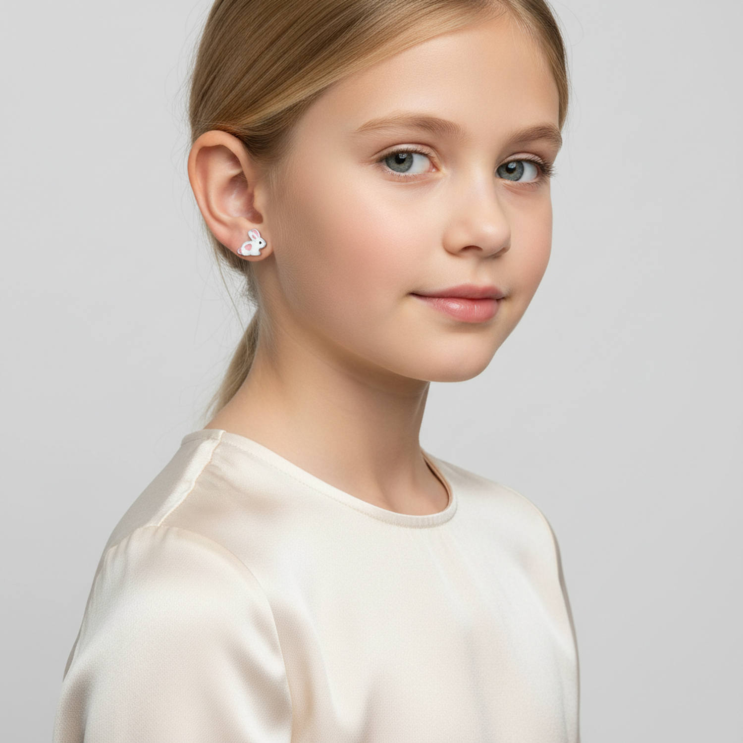 Young girl wearing sterling silver rabbit earrings for kids by Melchior Jewellery on a grey background