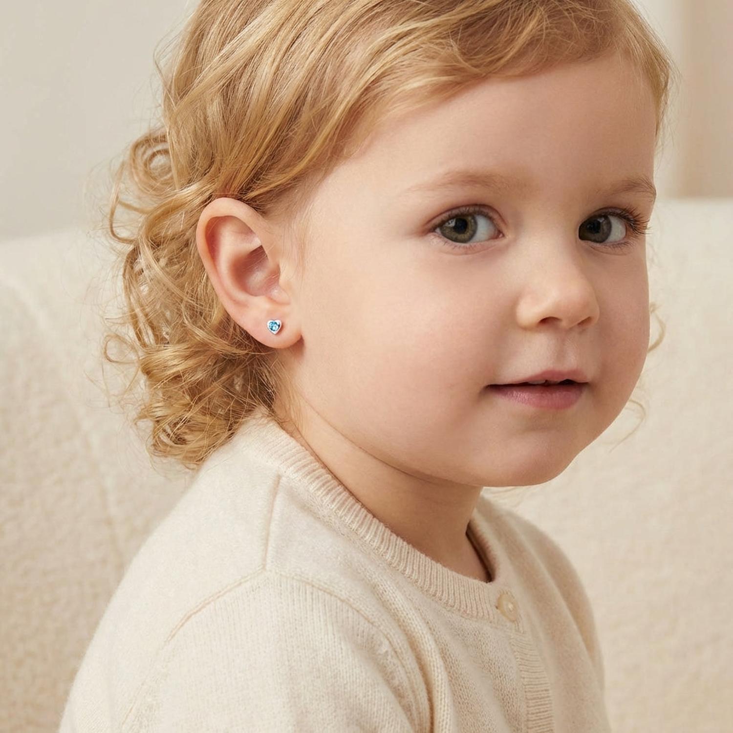 Young child wearing blue crystal heart stud earrings for kids by Melchior Jewellery close up