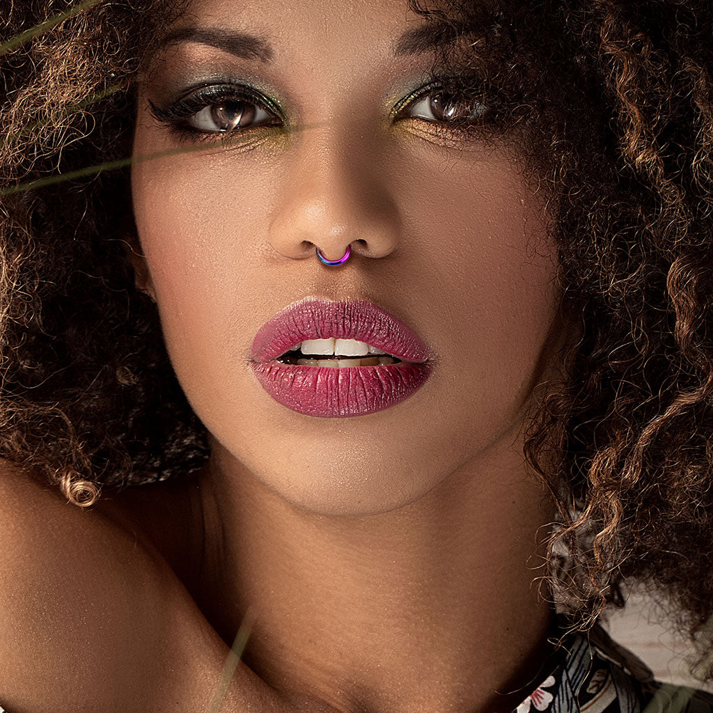 Melchior Jewellery coloured steel segment ring septum on model with curly hair bold eye makeup and mauve lips
