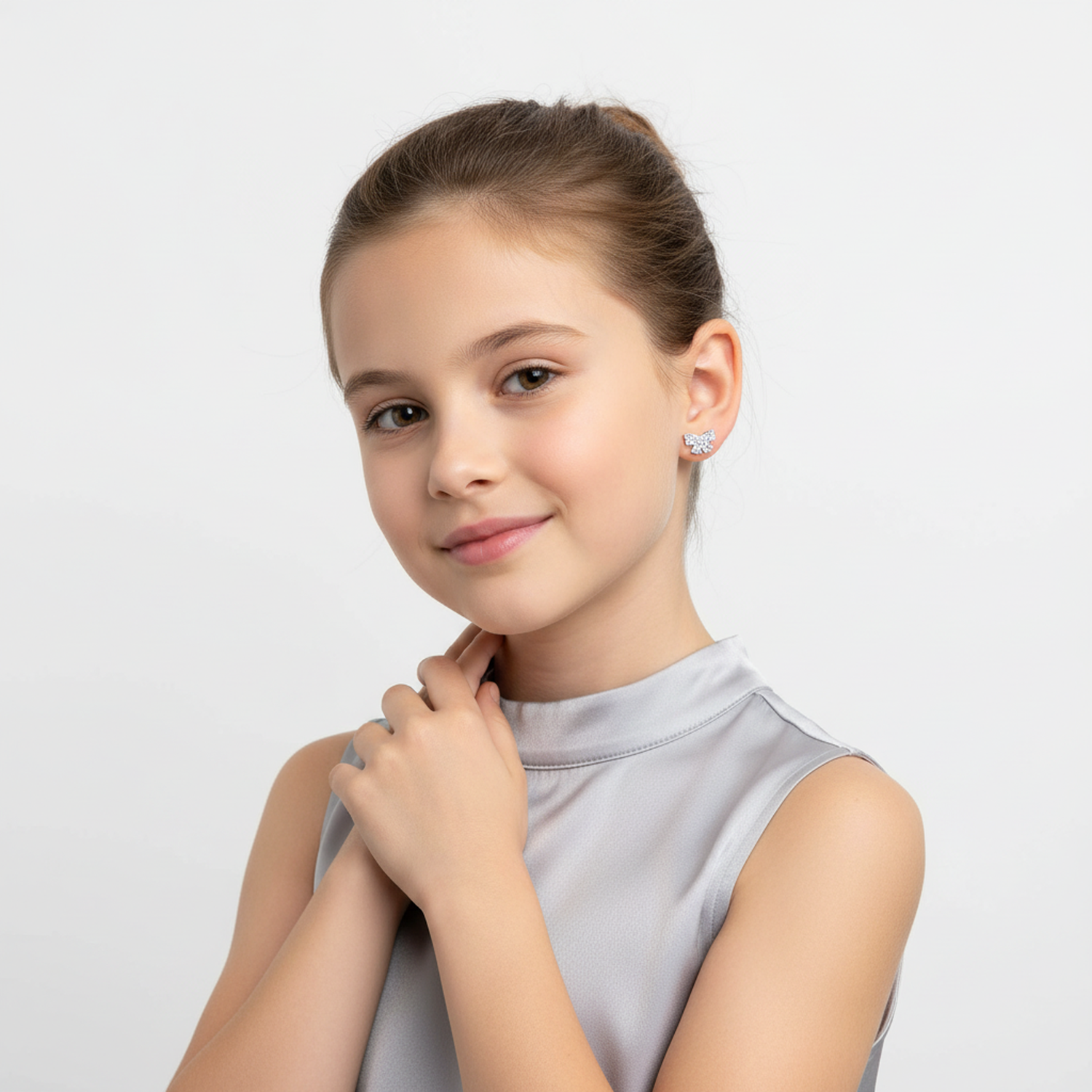 Girl wearing Melchior Jewellery crystal bow earrings for kids with a silver sleeveless top