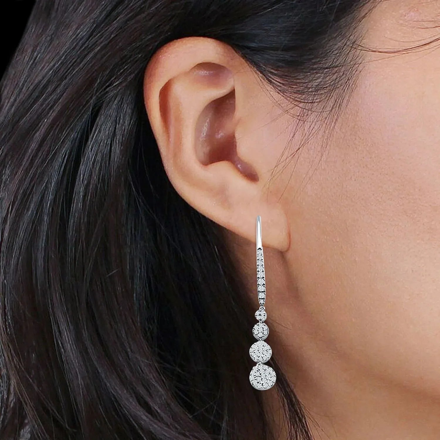 Silver cubic zirconia drop earrings with four round stones in graduated sizes worn on woman's ear
