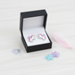 Cute silver unicorn earrings for children displayed in black Melchior Jewellery box with decorative stars and pink feather