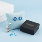 Melchior Jewellery flower stud earrings for children with blue and clear stones displayed on a blue cushion with a black gift box