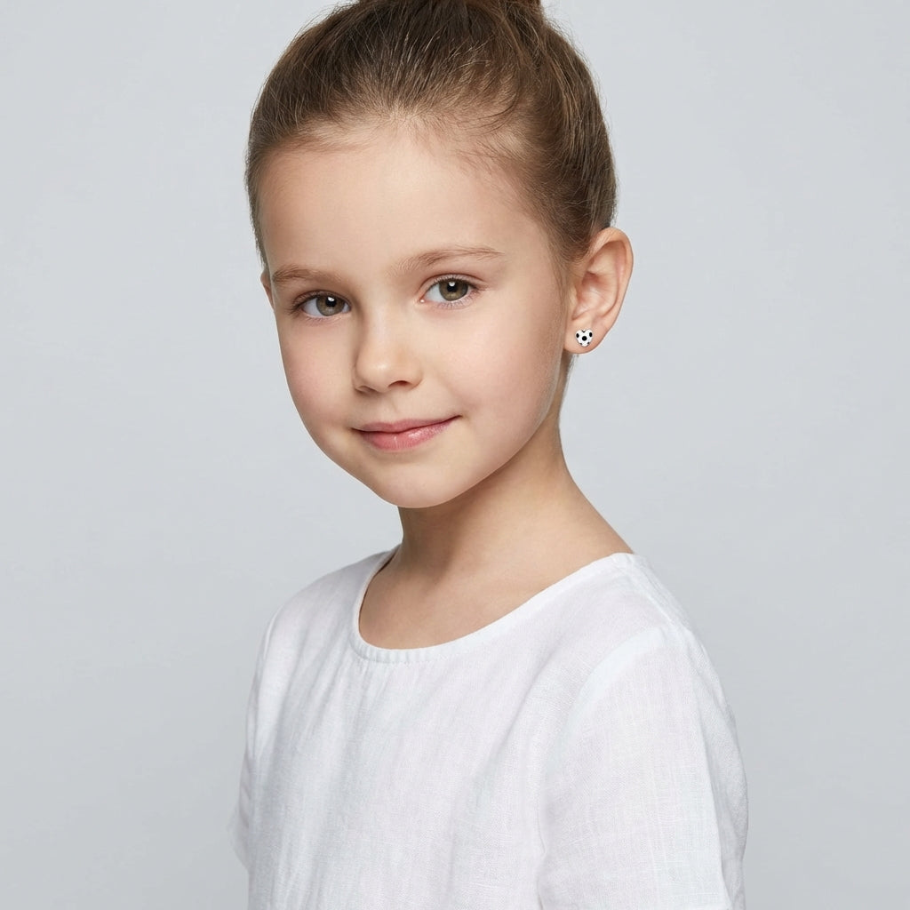 Young girl wearing Melchior Jewellery football earrings for girls in white and black design