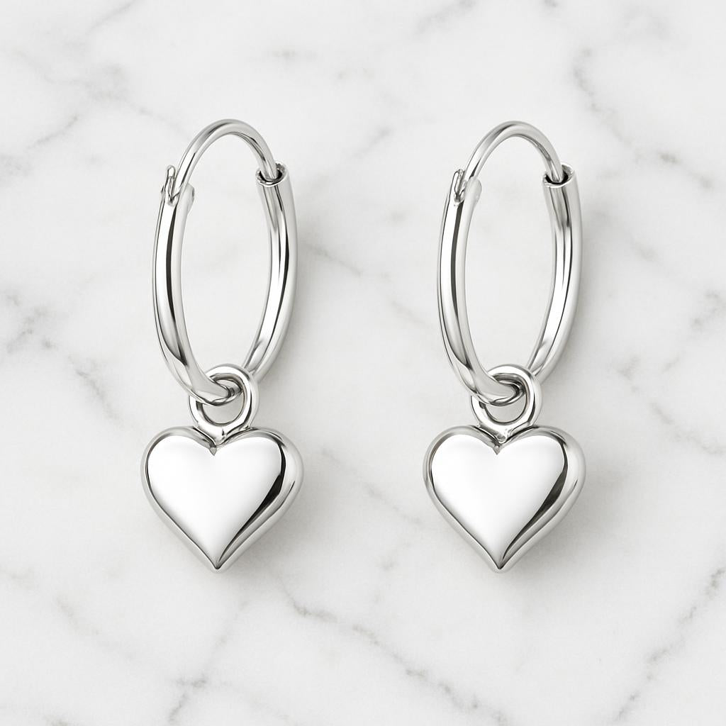 Girls silver hoop earrings with heart charm by Melchior Jewellery on white marble background