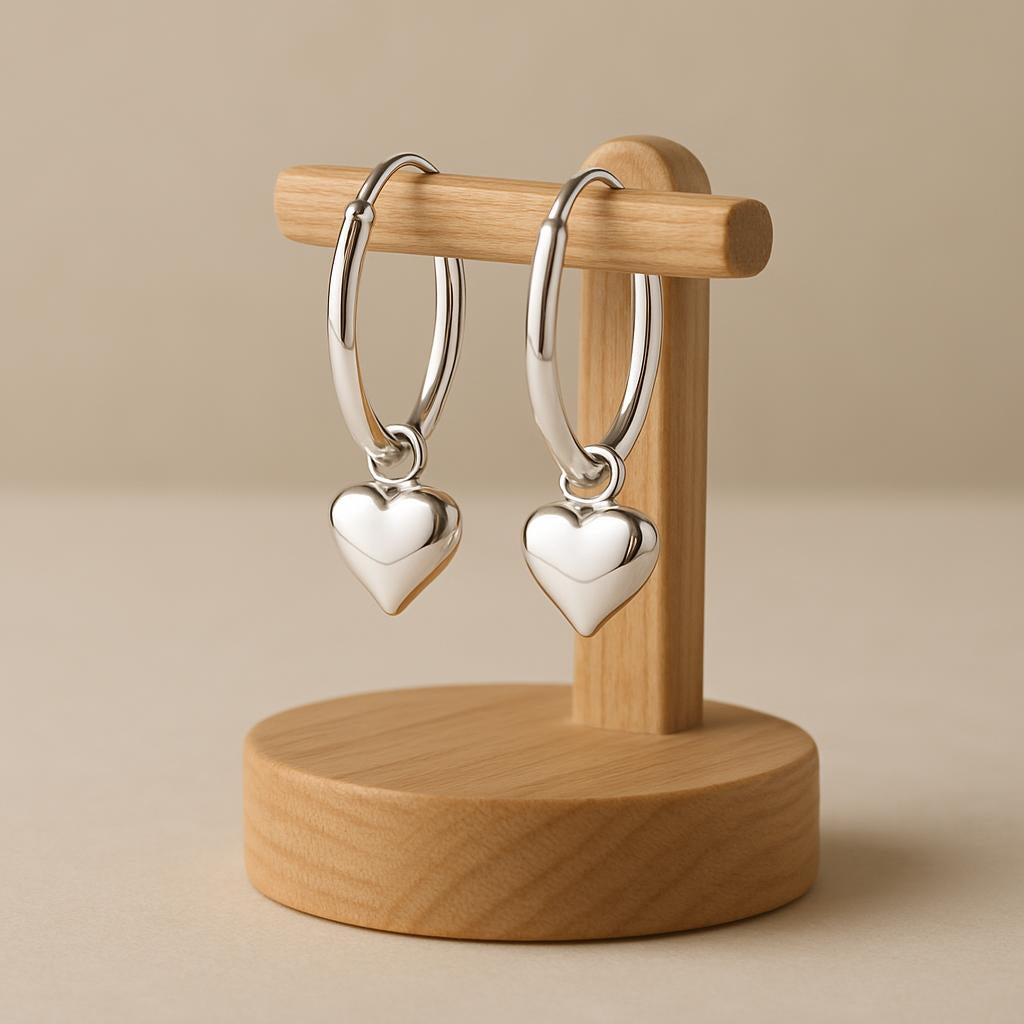 Girls silver hoop earrings with heart charm displayed on a wooden stand by Melchior Jewellery