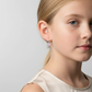 Heart-shaped silver earrings for children worn by young girl with blonde hair and white top